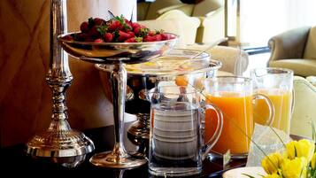 Un bufé de desayuno con diversas frutas, bebidas y una pieza central decorativa de plata.