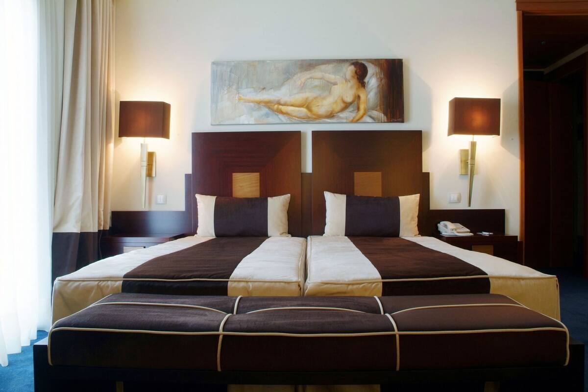 Cama doble con cabecera, dos mesitas de noche, un cuadro sobre la cama y una lámpara a cada lado.