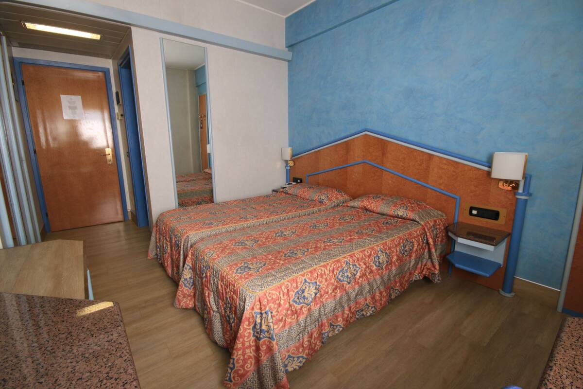 A hotel room with a bed, bedside tables, a door, and a mirror.