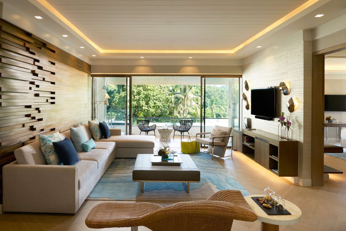 Un salon moderne avec un canapé, une table basse et des fauteuils en osier. Il y a un balcon avec vue sur la verdure.