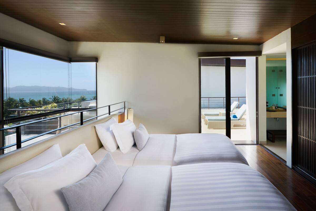 Une chambre d’hôtel moderne dotée d’un grand lit, d’un balcon avec vue sur la mer et d’une salle de bain séparée.