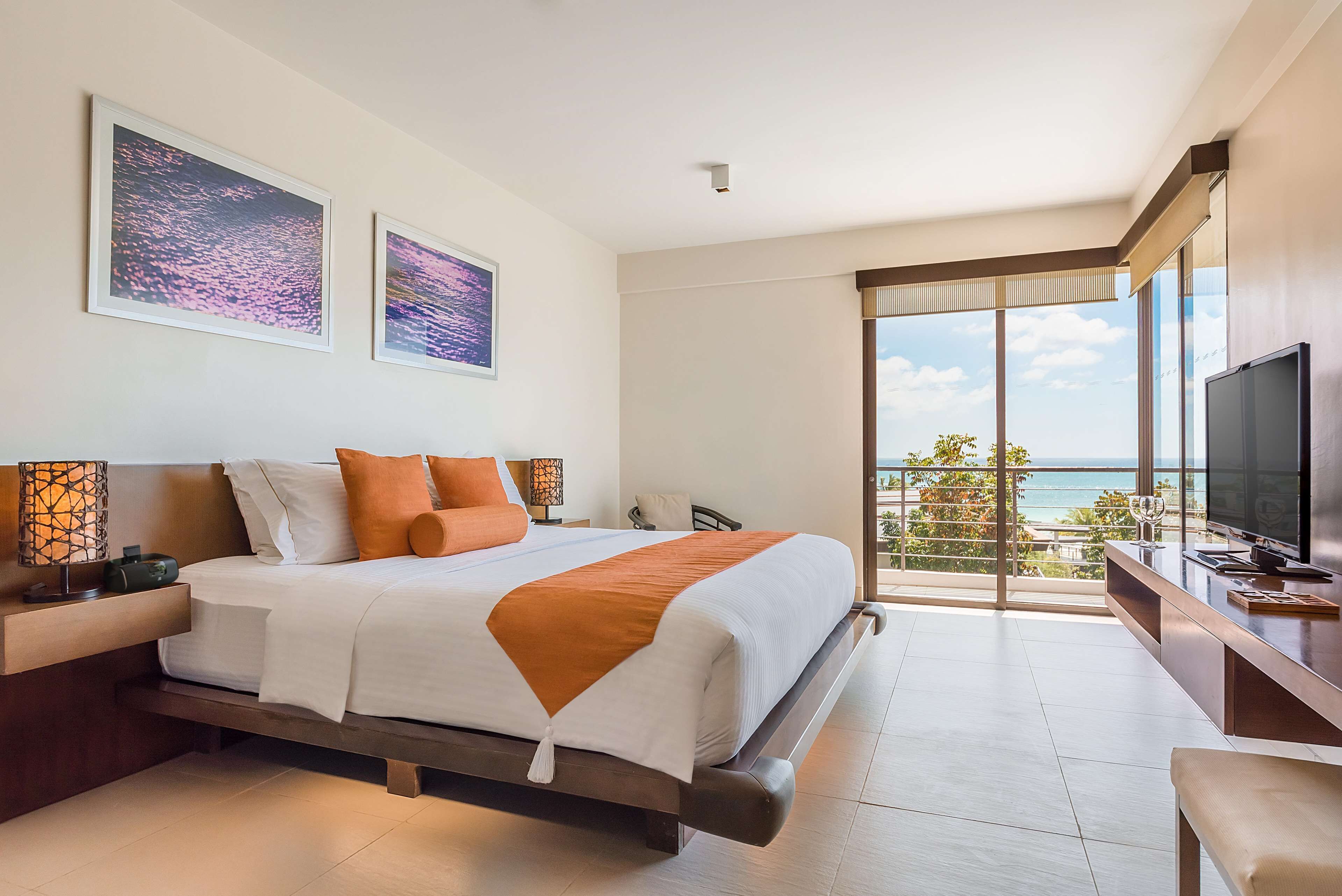A modern hotel room with a large bed, a TV, and a balcony with a view of the ocean.