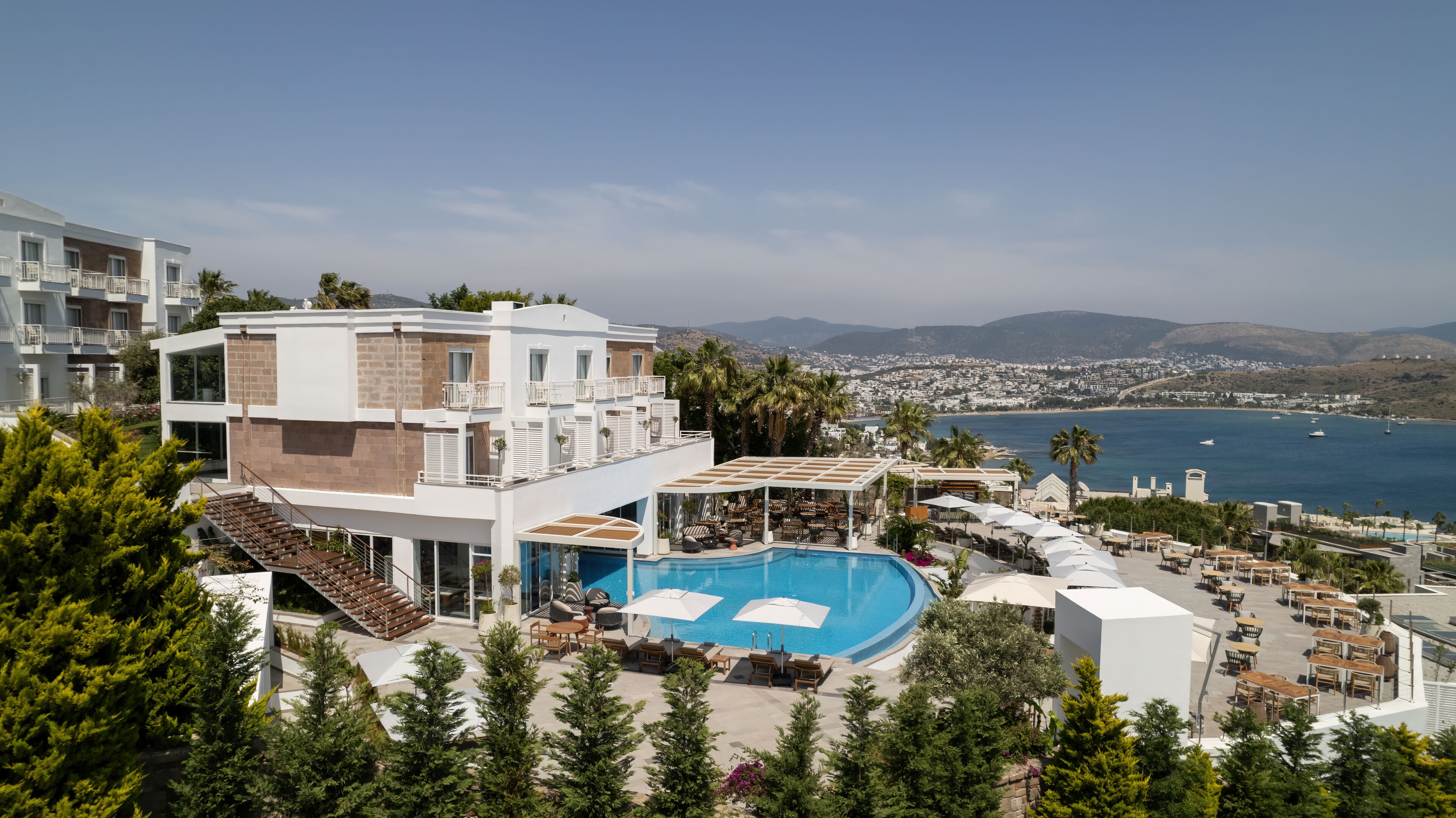 Un hôtel moderne doté d’une piscine sur le toit, d’un espace extérieur aménagé et offrant une vue sur la mer et le paysage urbain.