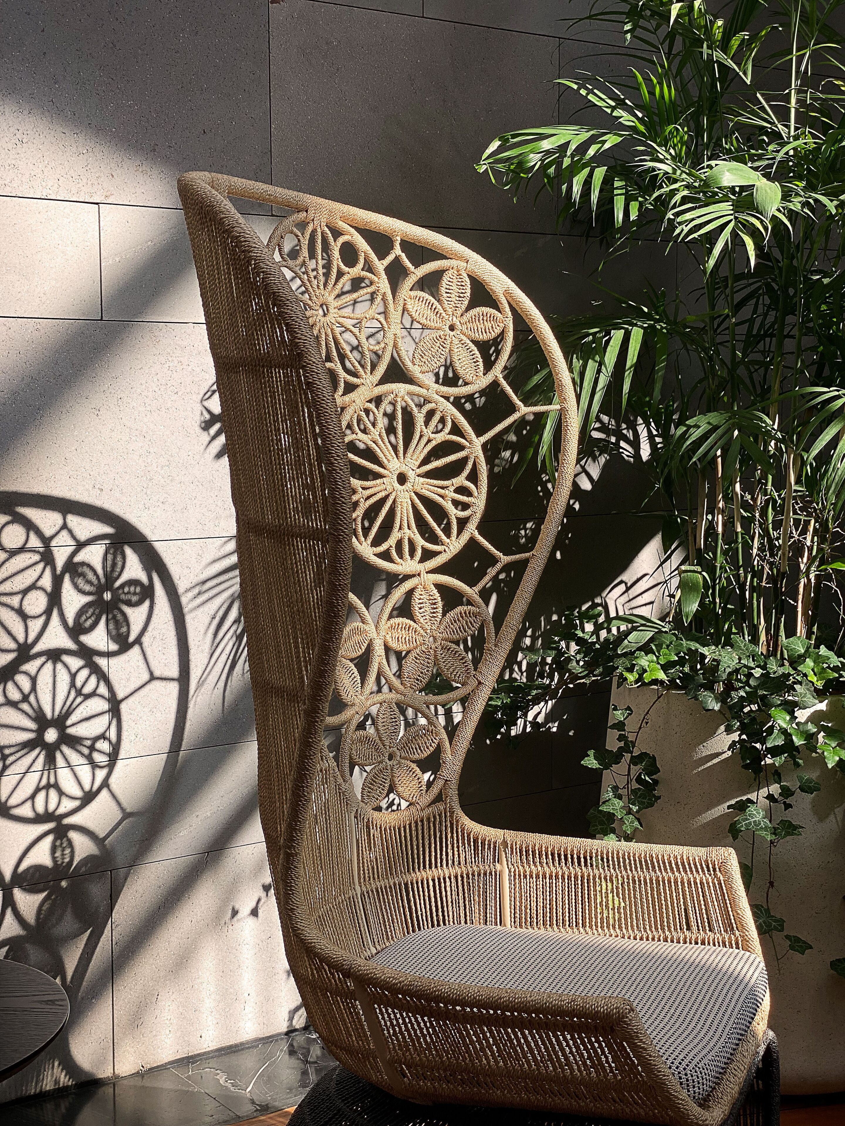 A wicker chair with intricate patterns, positioned against a wall with a shadow of a decorative metalwork.