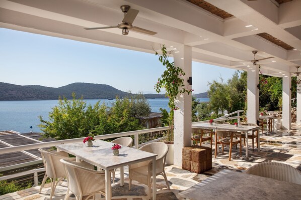 A covered outdoor seating area with tables and chairs, overlooking a body of water and hills. - Doria Hotel Bodrum-City Center (Bodrum)