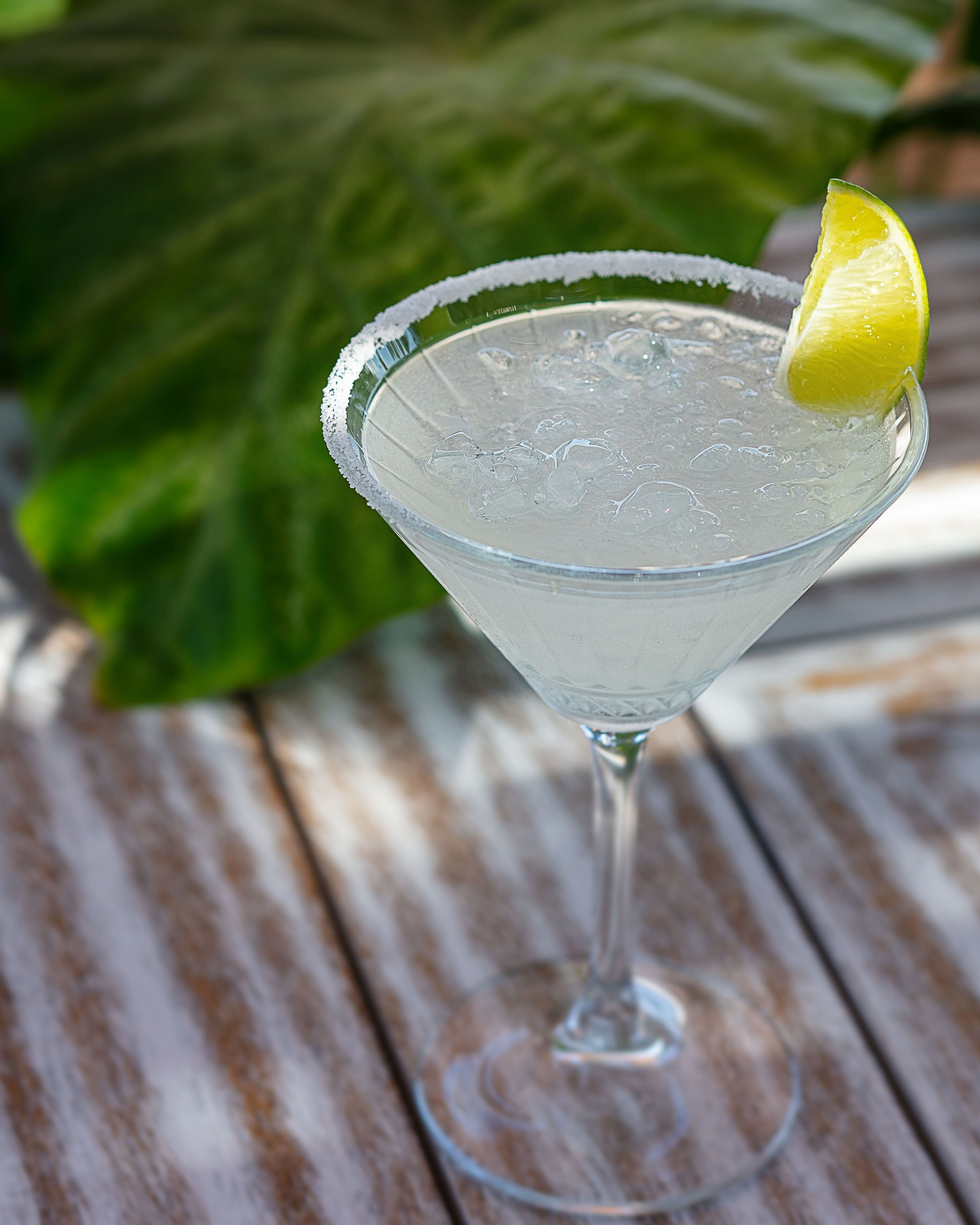 A clear glass cocktail with ice and a lime garnish on a wooden table.