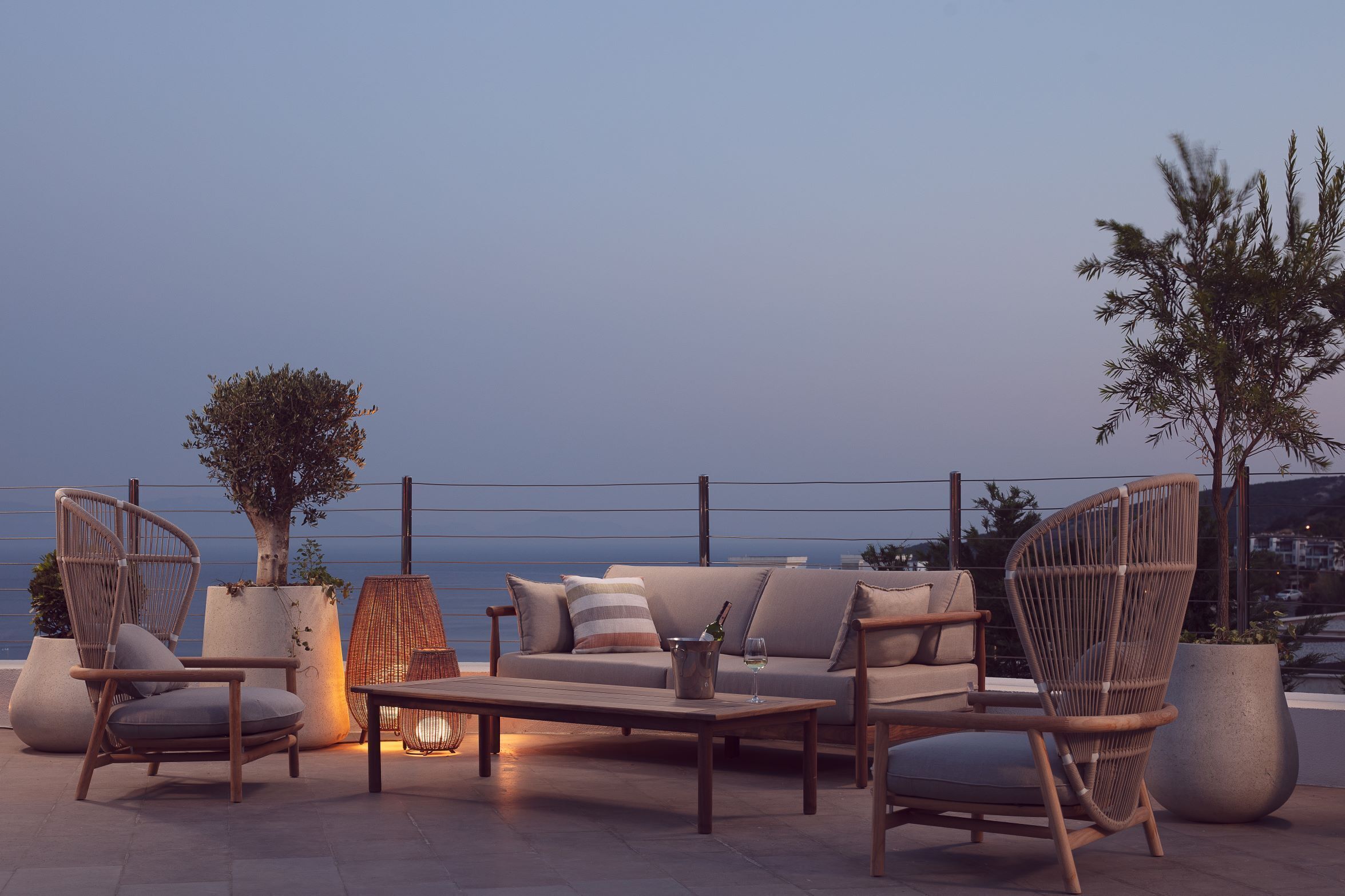 A terrace with wicker furniture, a sofa, and a table, overlooking a body of water.