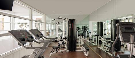 Un gimnasio con cintas de correr, máquinas de pesas y un espejo grande.