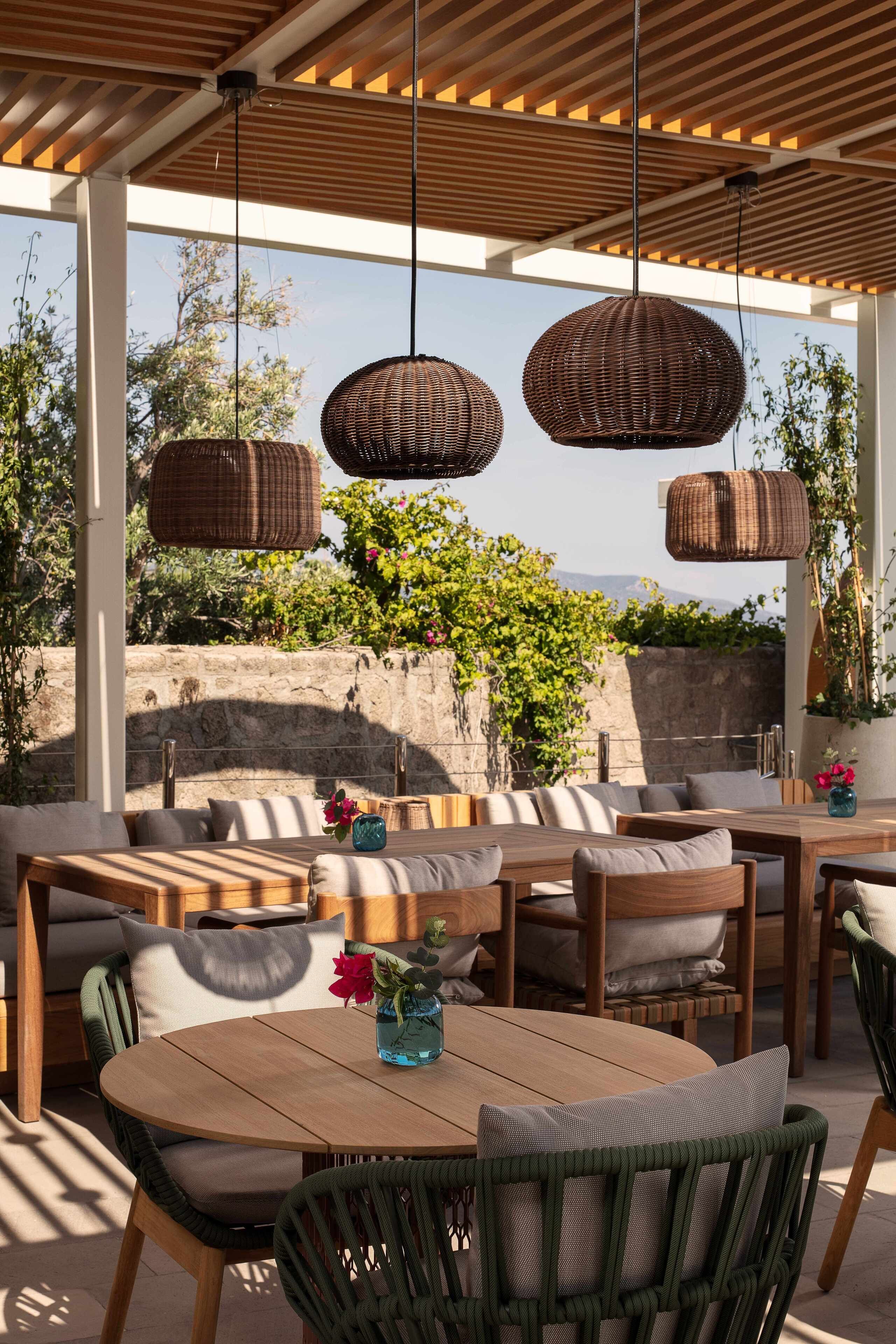 Un patio al aire libre con luces colgantes de mimbre, mobiliario de madera y vistas a zonas verdes y montañas.