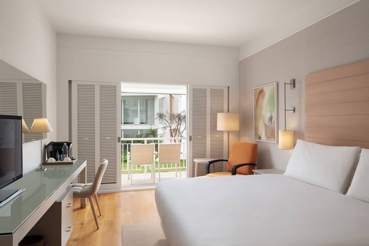 Une chambre d’hôtel avec un lit, un bureau, des chaises et un balcon offrant une vue.