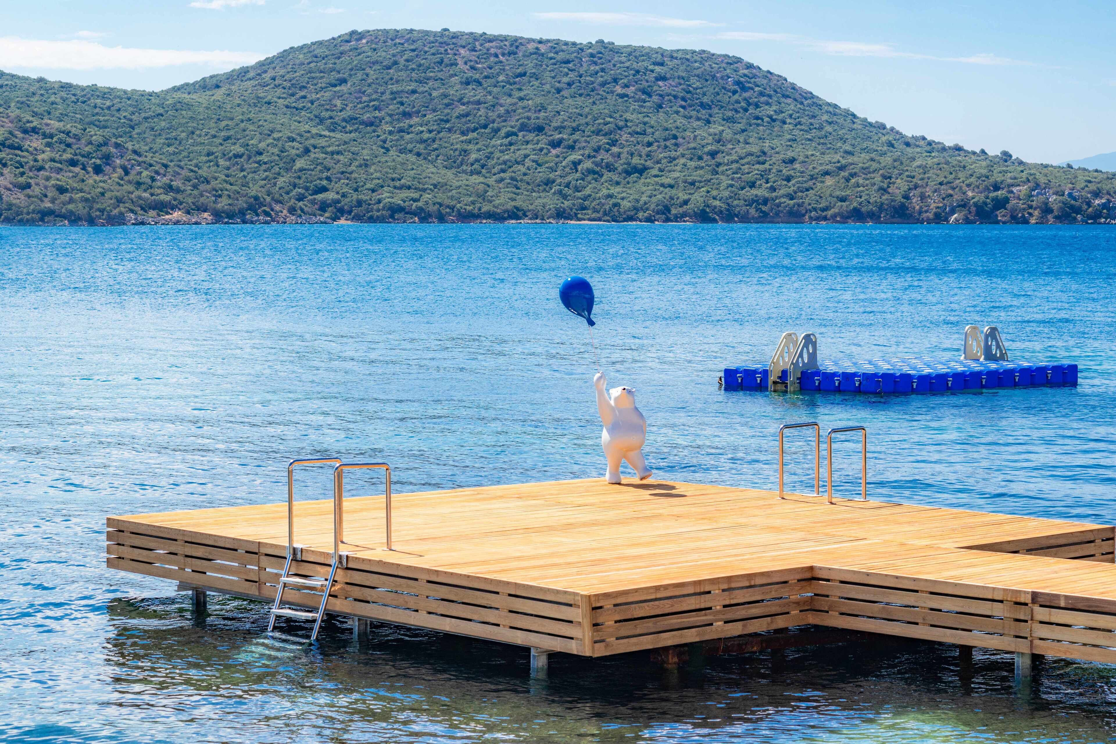 A wooden dock extending into a calm lake with a clear view of a forested hill in the background.