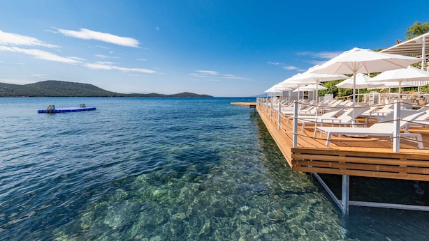 A wooden deck with white lounge chairs and umbrellas extending over a clear blue lake. -  Doria Hotel Bodrum-City Center (Bodrum)