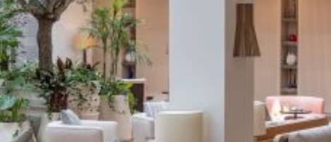 Un espace intérieur moderne doté d’un coin salon avec des canapés et une table basse, le tout agrémenté de plantes et d’un arbre.