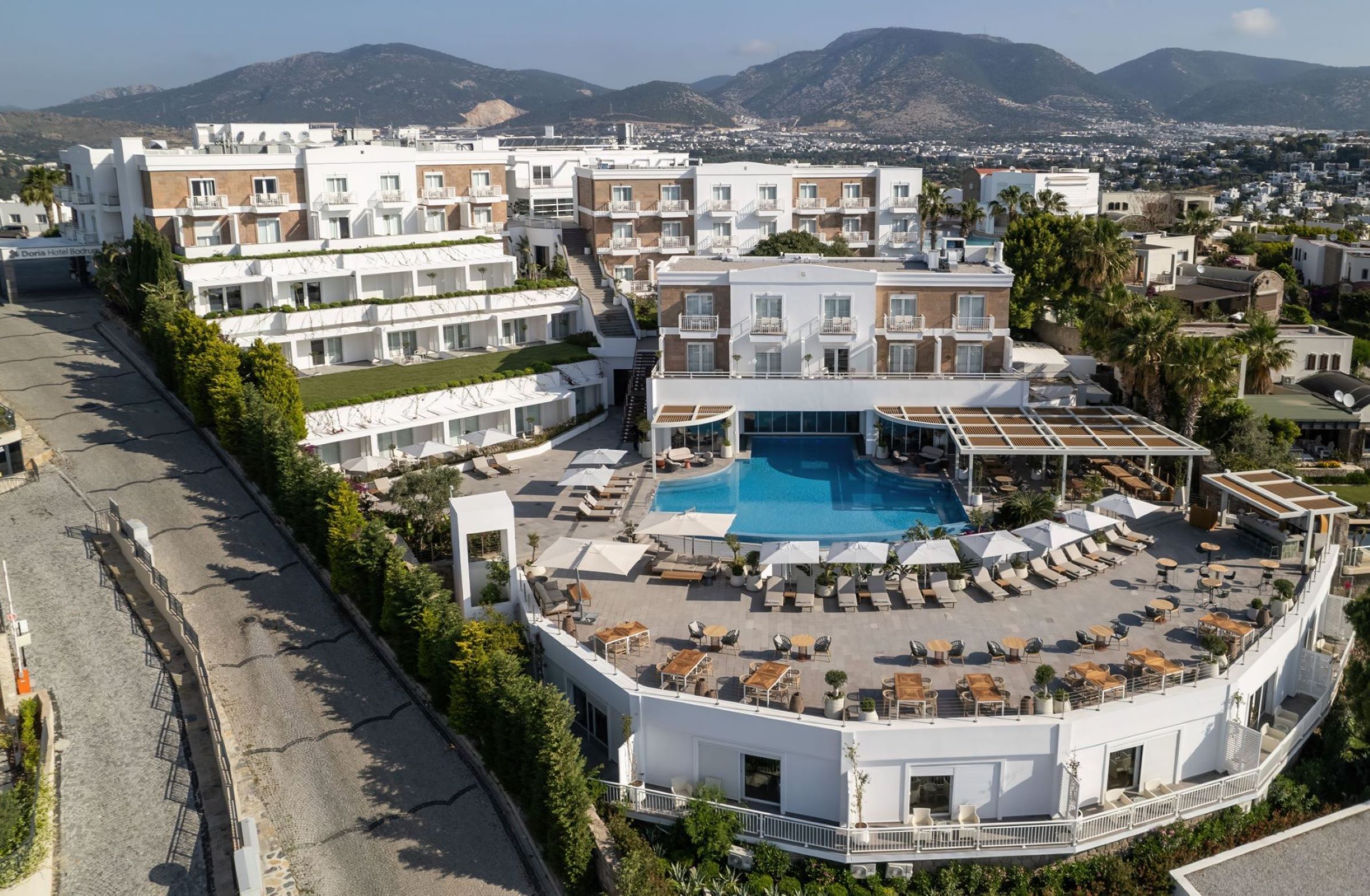 A hotel with a rooftop pool, multiple balconies, and a view of the surrounding city and mountains.