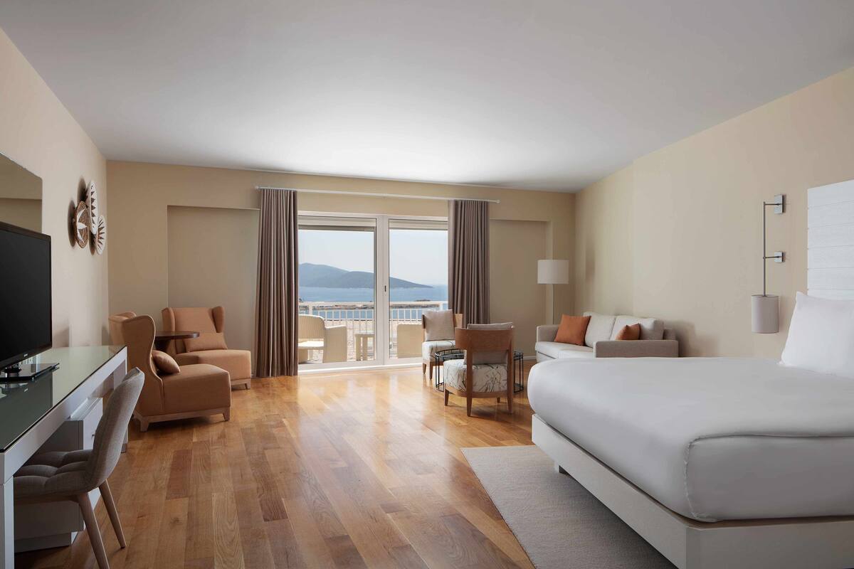 Une chambre d’hôtel équipée d’un lit, d’un bureau, d’une chaise, d’un canapé et d’un balcon avec vue.