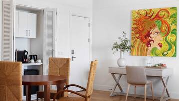 A modern room with a dining table, wicker chairs, a white desk, and a colorful abstract painting.