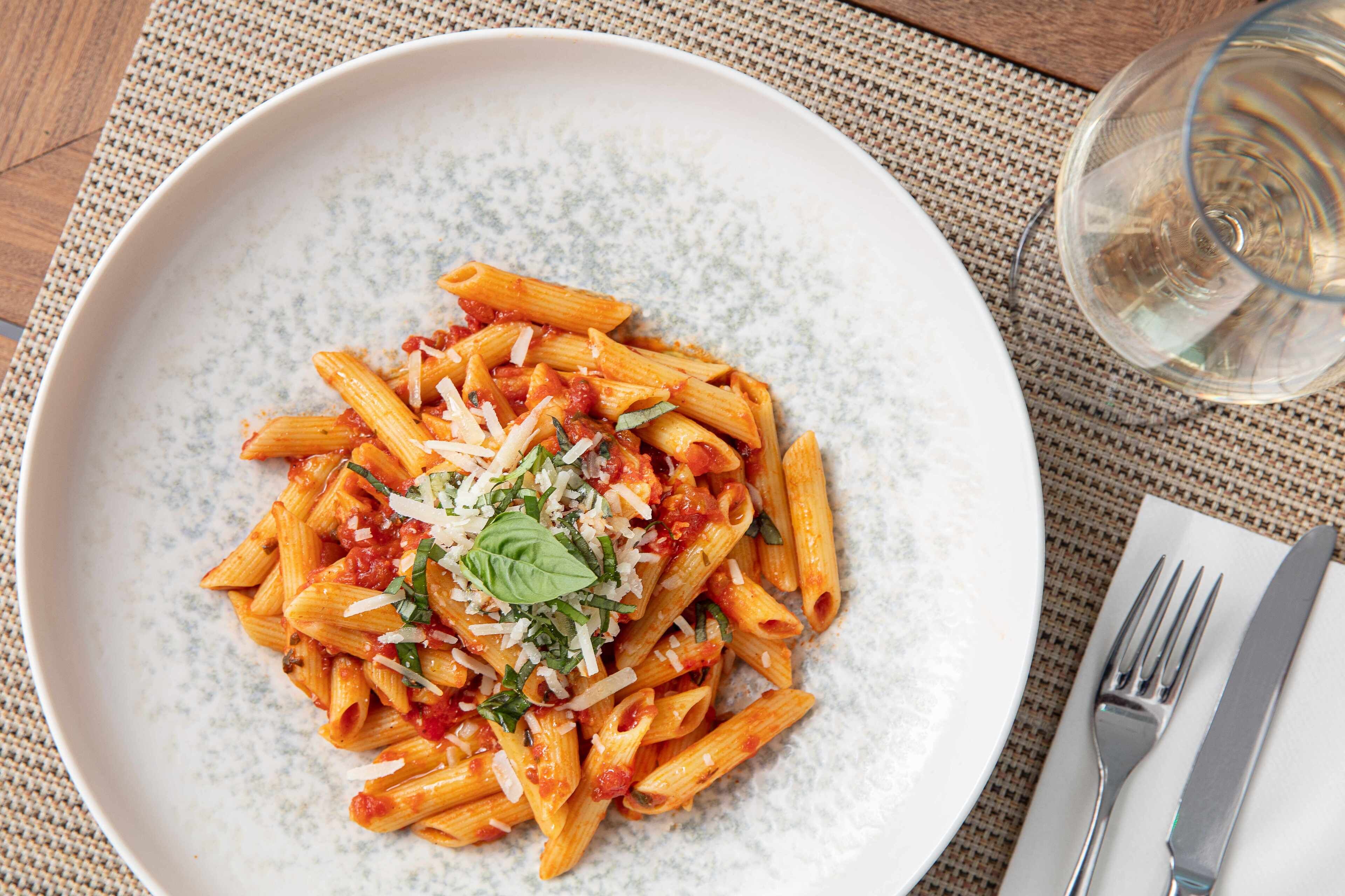 Un plato de pasta penne con salsa de tomate, queso y albahaca.