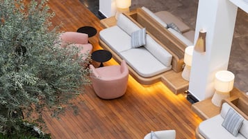 A modern lounge area with wooden flooring, multiple seating options including sofas and chairs, and potted plants.