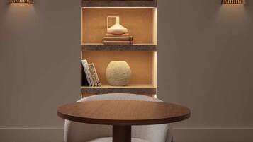 Un interior moderno con una mesa redonda y dos sillas, una estantería con objetos decorativos y dos lámparas de pared.