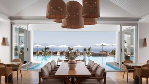 A modern dining area with a pool view, featuring a wooden table and chairs, wicker pendant lights, and a large vase with plants. -  Doria Hotel Bodrum-City Center (Bodrum)
