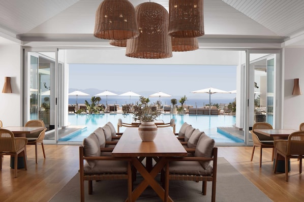 A modern dining area with a pool view, featuring a wooden table and chairs, wicker pendant lights, and a large vase with plants. - Doria Hotel Bodrum-City Center (Bodrum)