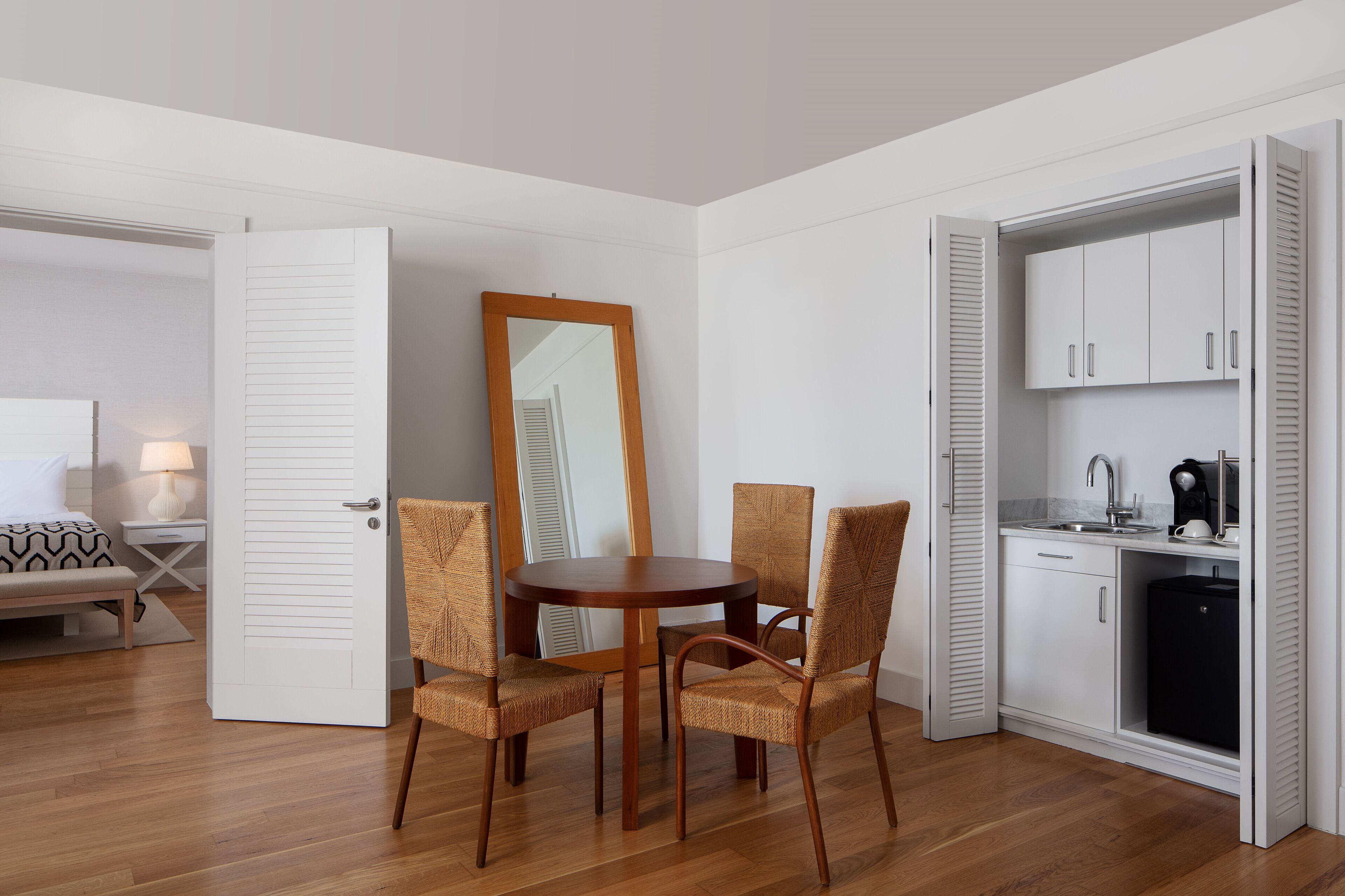 Une pièce compacte comprenant une table à manger et des chaises, un petit coin cuisine et un lit recouvert d’une courtepointe à motifs.