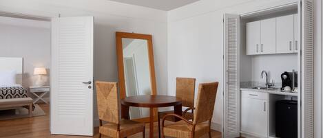 Une pièce compacte comprenant une table à manger et des chaises, un petit coin cuisine et un lit recouvert d’une courtepointe à motifs.