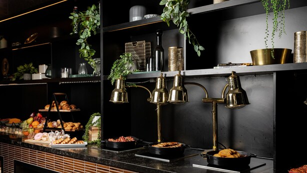 A buffet setup with various food items, including pastries and fruits, and decorative elements like plants and metallic containers. - Rydges Campbelltown (Campbelltown)