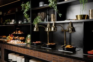 A buffet setup with various food items, including pastries and fruits, and decorative elements like plants and metallic containers.