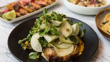 A plate of food with sliced apples and greens on top of a piece of meat.