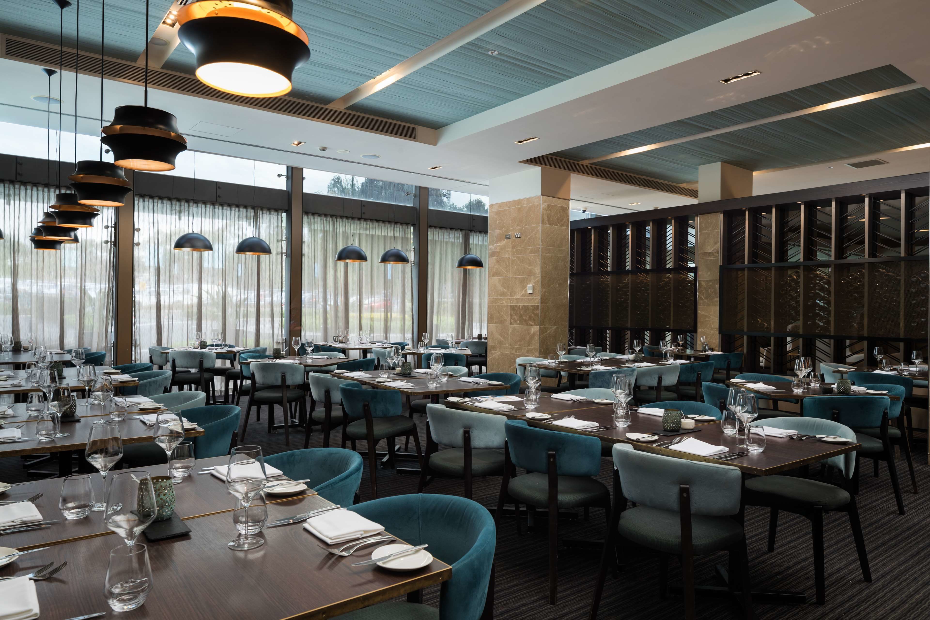 Ein Restaurant mit mehreren gedeckten Tischen, das durch ein modernes Interieur mit blauen Stühlen und Pendelleuchten besticht.
