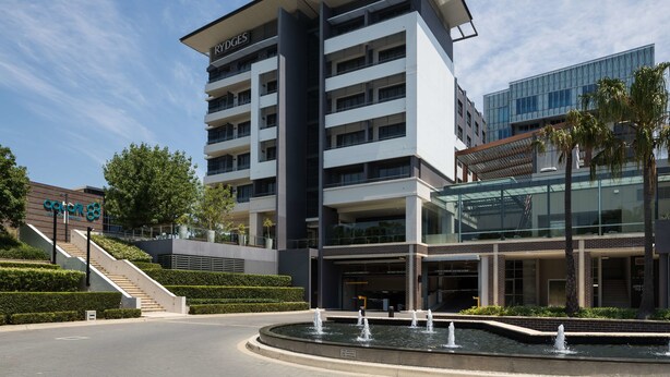 A modern hotel with a central courtyard featuring a fountain, surrounded by well-maintained landscaping and a staircase leading to the entrance.