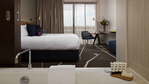 A hotel room with a bed, a desk, a chair, a bathtub, and a window with curtains.