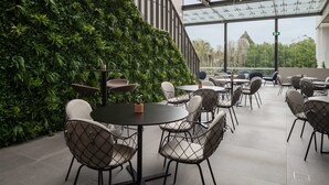 A modern indoor dining area with round tables and chairs, surrounded by a lush green wall. - Rydges Campbelltown (Campbelltown)