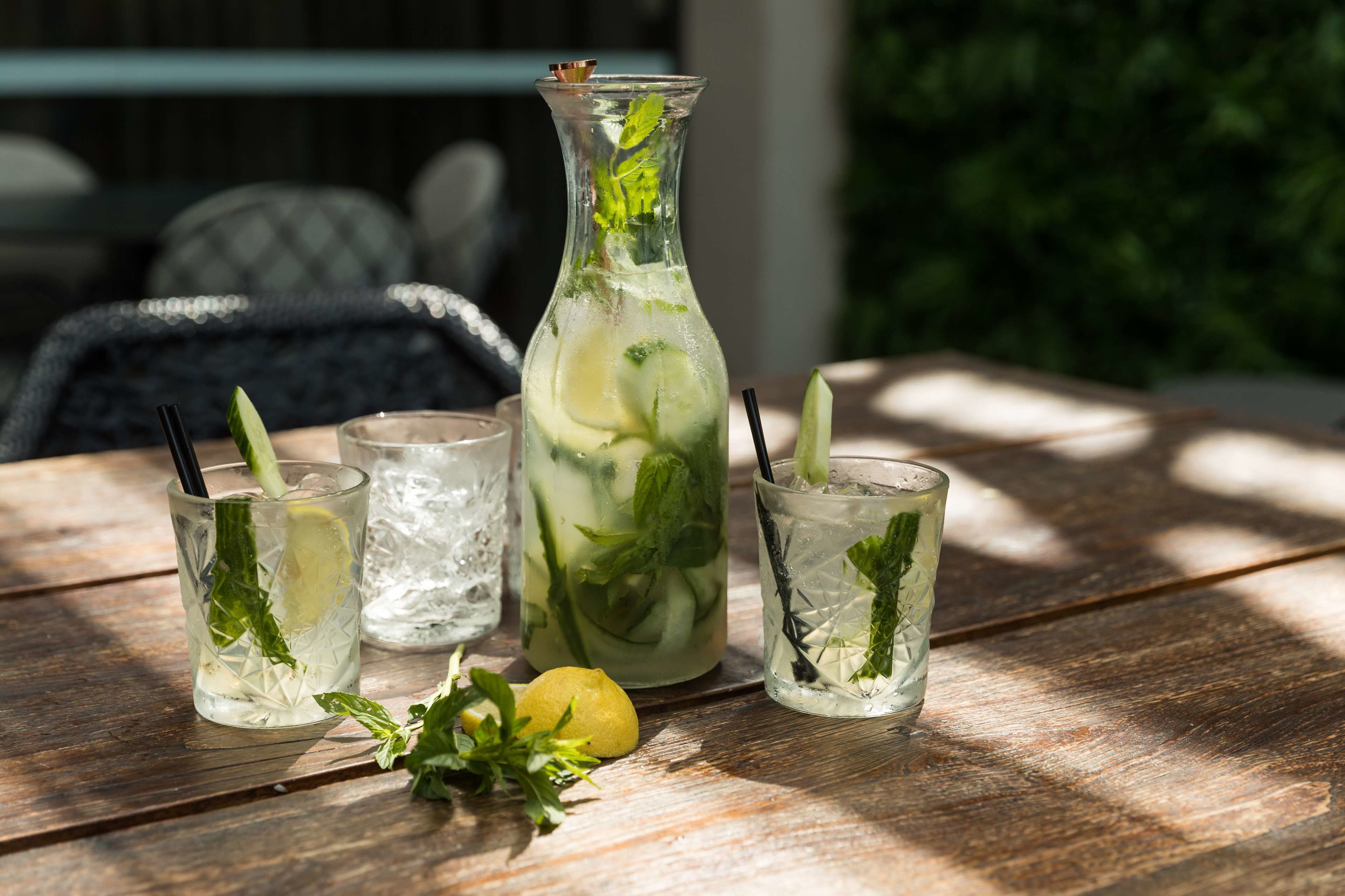 Una mesa de madera con tres vasos de una bebida refrescante de menta, una jarra y un limón.