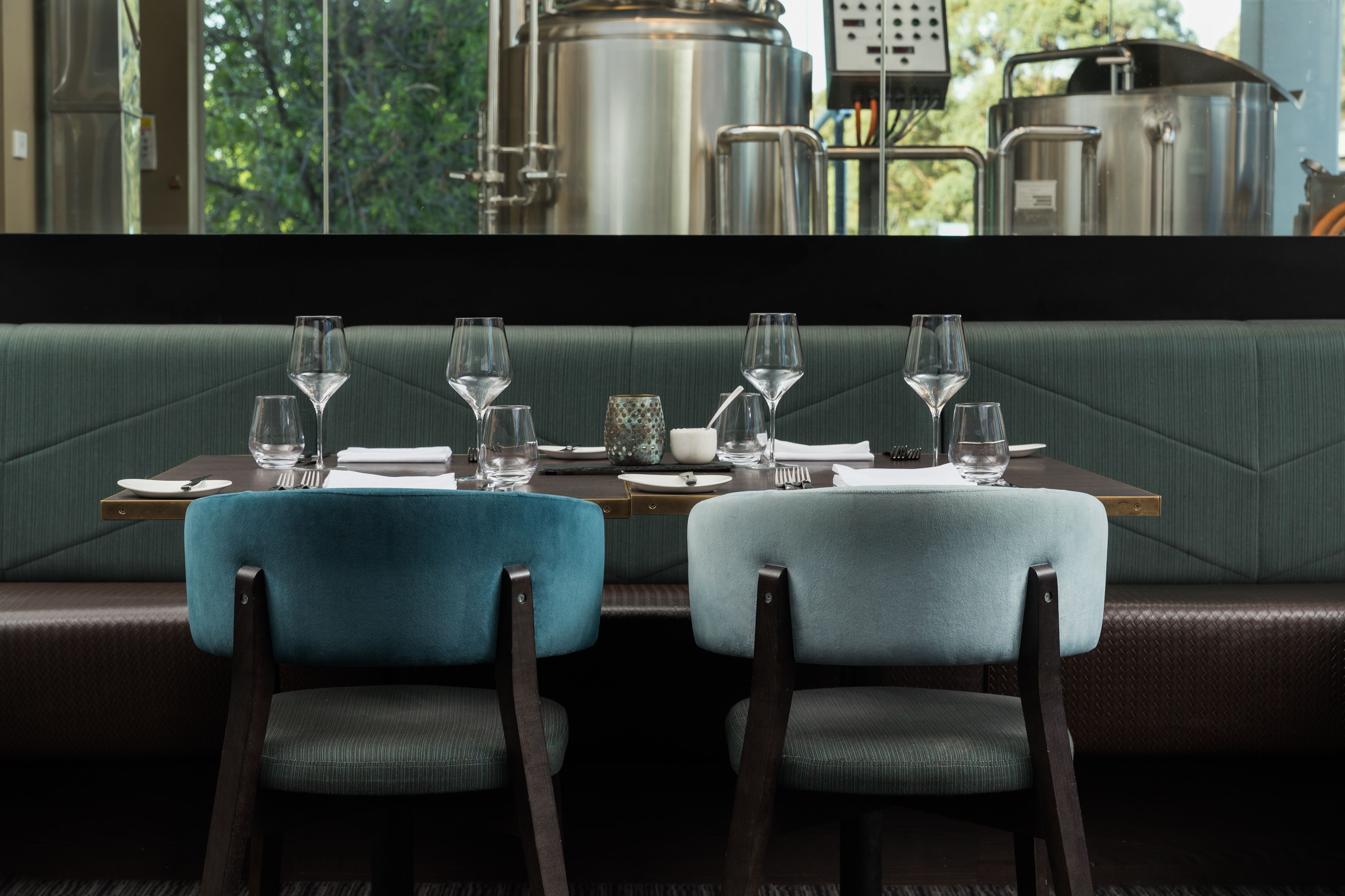 Une banquette de restaurant avec deux chaises, une table dressée avec des verres à vin, des assiettes et des couverts.