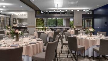 Un restaurante moderno con mesas redondas dispuestas para comer, con una paleta de colores neutros e iluminación natural gracias a amplias ventanas.