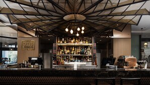 A bar area with a modern design, including a ceiling with geometric patterns and hanging lights. - Rydges Campbelltown (Campbelltown)