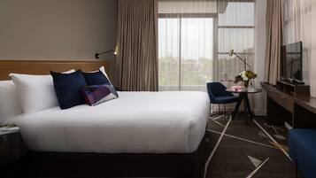 Habitación de hotel con una cama grande, un escritorio con silla, un televisor y una ventana con cortinas.