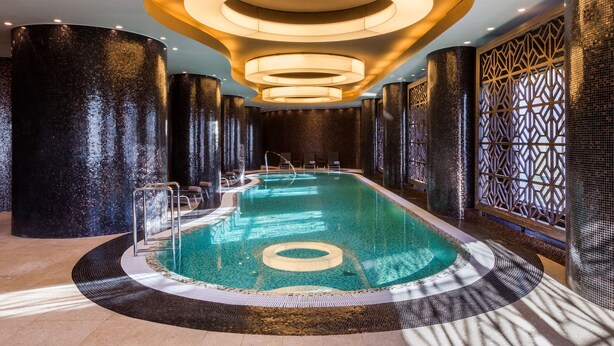 A modern indoor swimming pool with a circular design, surrounded by high, textured walls and a patterned floor.