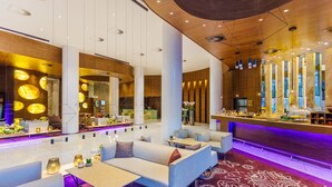 A modern hotel lobby with seating areas, a bar, and a reception desk.