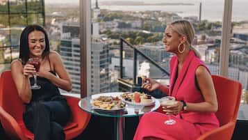 Two women seated at a table with a city view, holding drinks and eating.