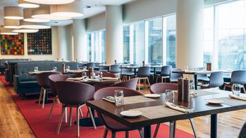 A modern restaurant with multiple dining tables and chairs, large windows, and a red carpet.