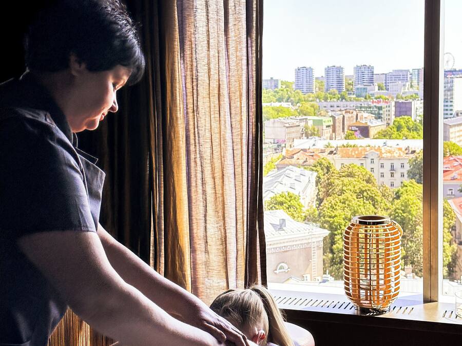 Eine Massagebehandlung in einem Raum mit großem Fenster und Blick auf eine Stadtlandschaft.