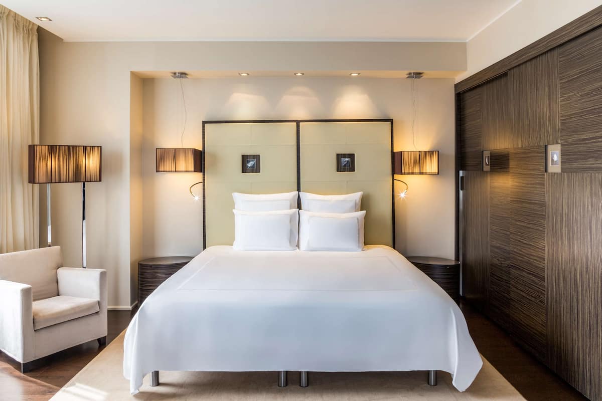 A modern hotel room with a large bed, two bedside lamps, a chair, and a wooden accent wall.