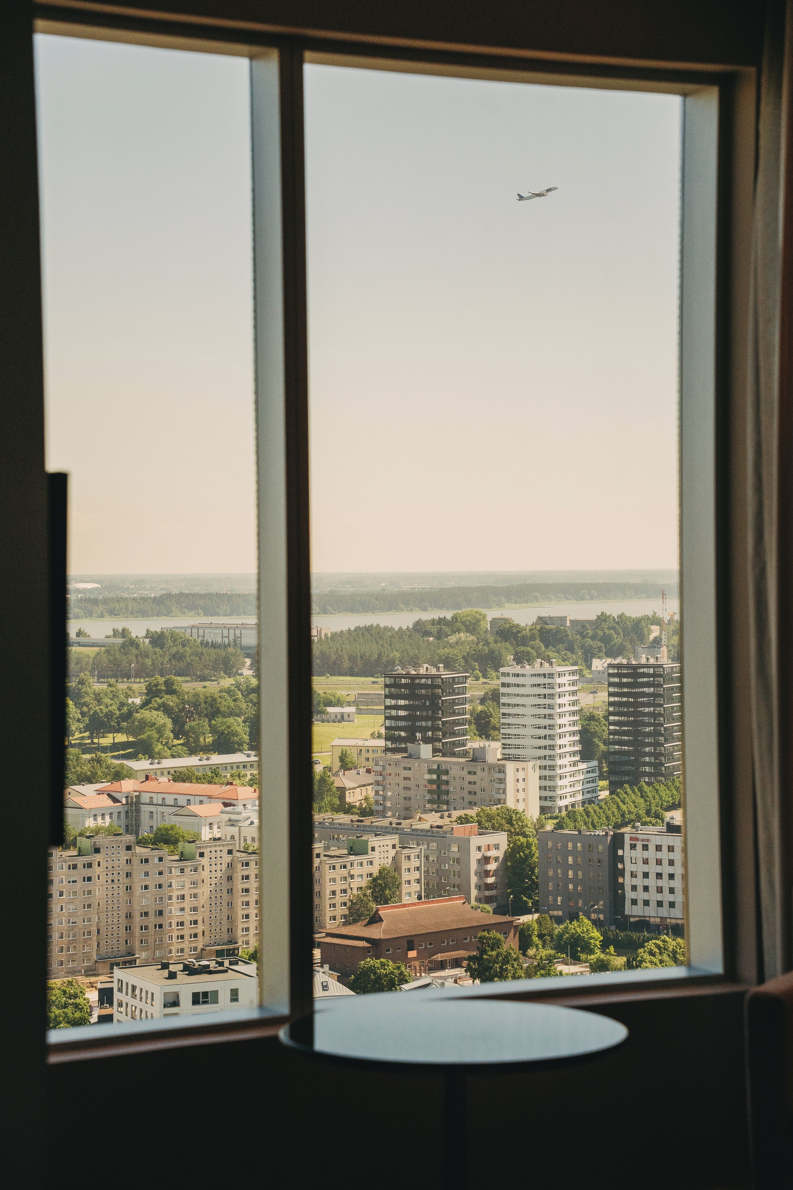 A view from a window overlooking a cityscape with buildings, a river, and a clear sky.