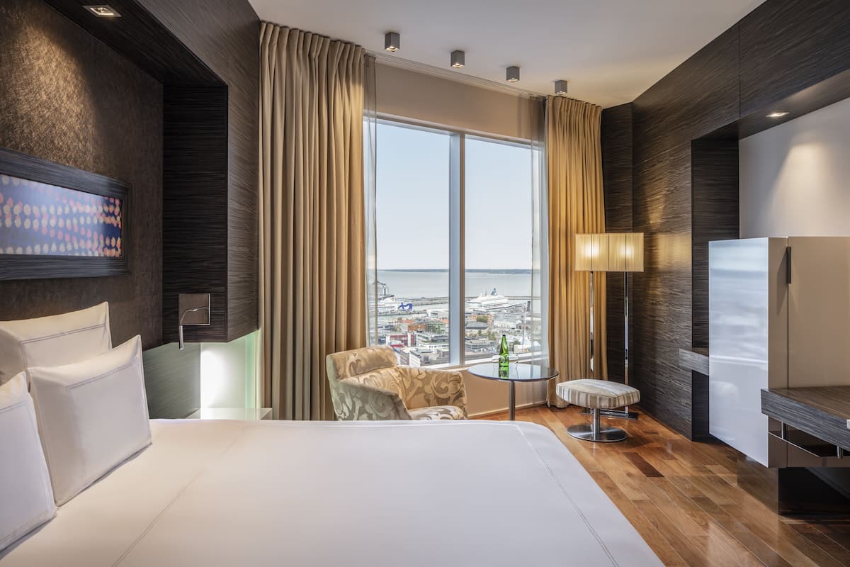 A modern hotel room with a large bed, a seating area with a view of the city, and a television.