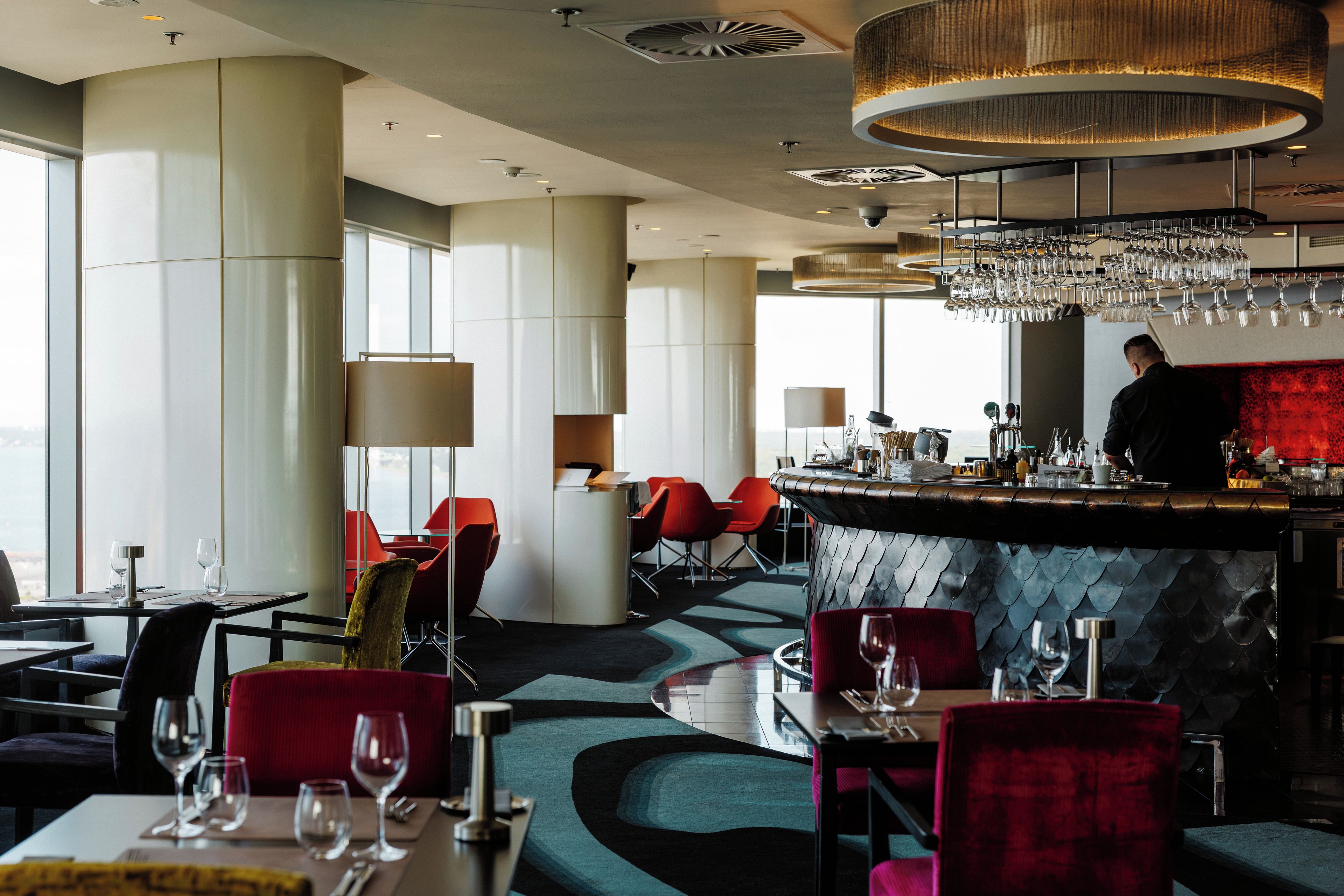 A modern restaurant interior with a bar area, seating arrangements, and a view through large windows.