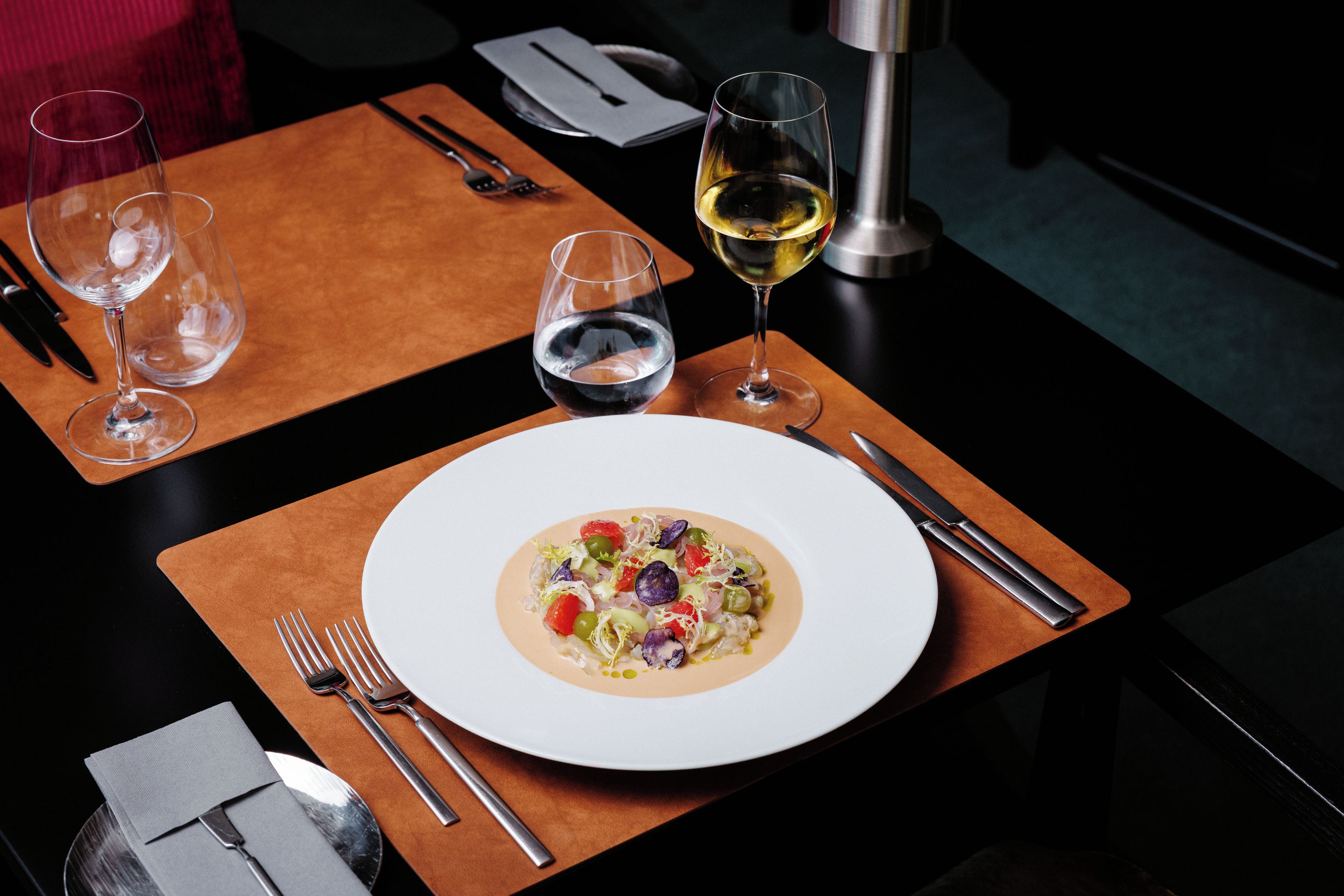 Une table à manger avec une assiette de nourriture, des couverts et deux verres de vin.