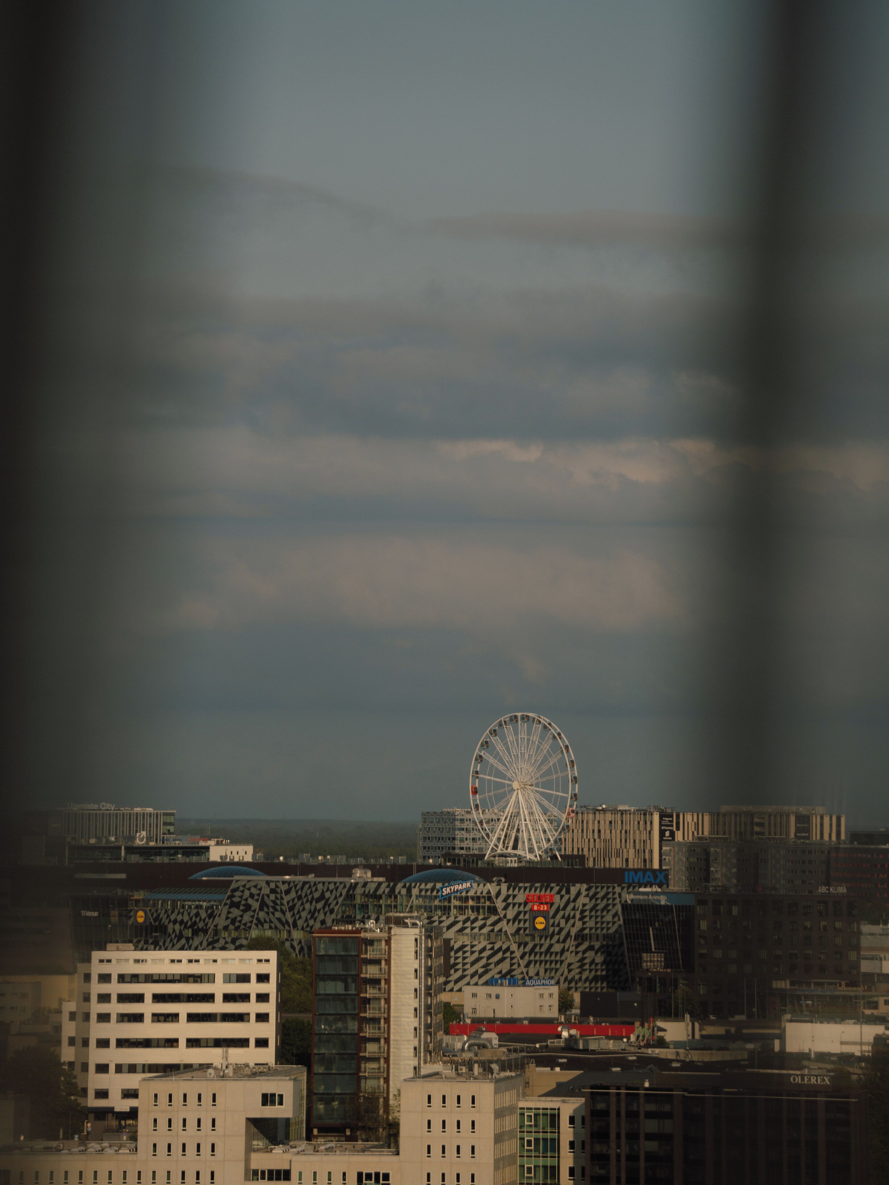 Paesaggio urbano con una ruota panoramica in evidenza, edifici moderni e cielo sereno.